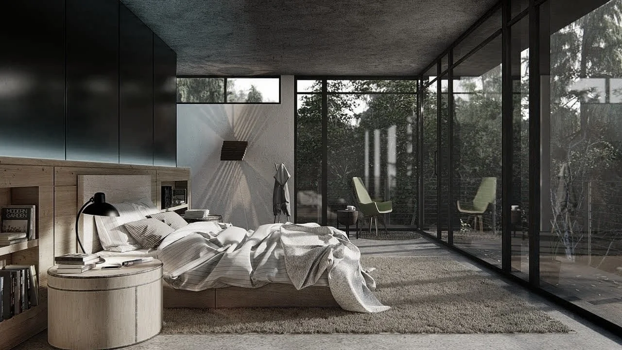 Modern bedroom with large glass windows looking outside at trees, a bed with a striped comforter, a round wooden nightstand with books and a black lamp, a wall-mounted light fixture, and two green chairs on a patio.