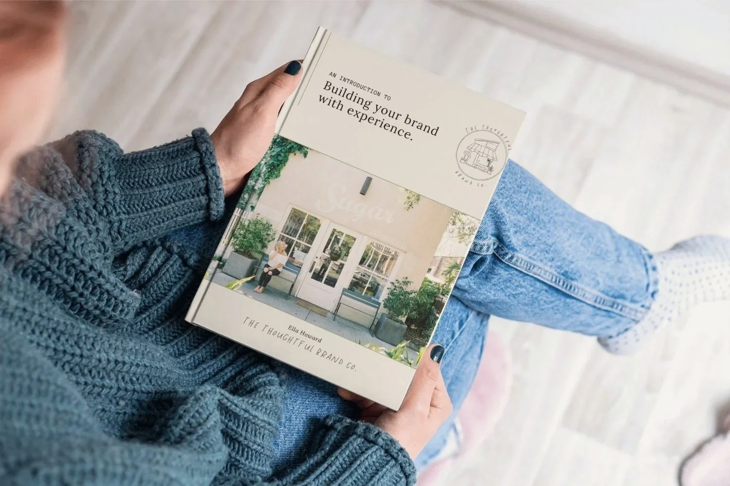 Person holding a book titled "Building your brand with experience" by Ella Howard, with a front cover image of a storefront and a person sitting outside
