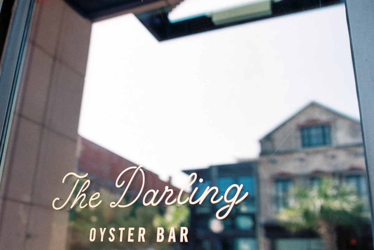 The reflection on a window shows a building, trees, and sky. The window has text that reads 'The Darling Oyster Bar'.