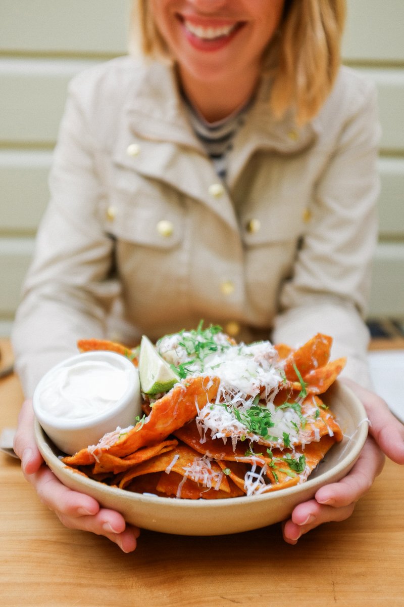 Ella holding a plate of fresh San Fran tortilla chips topped with cheese, sour cream, cilantro, and lime, with a side of guacamole.