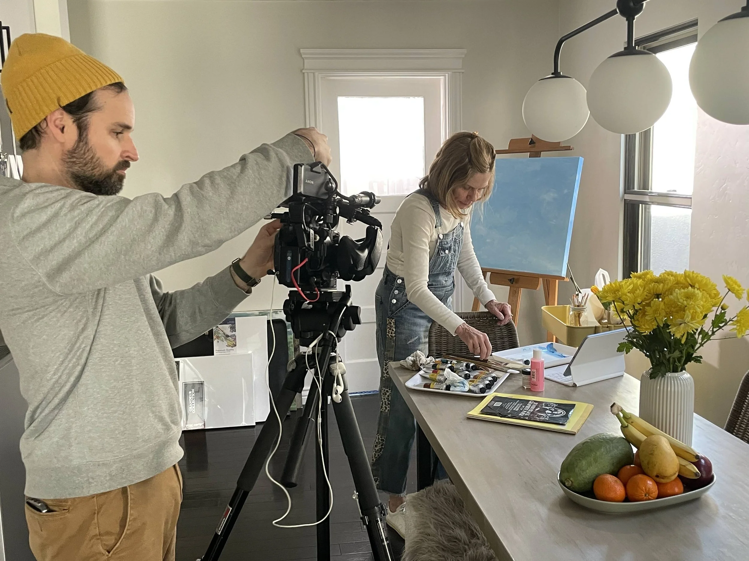 Ben filming "Un-Painted" —  The room is bright with windows, has an artist working on a canvas on an easel.