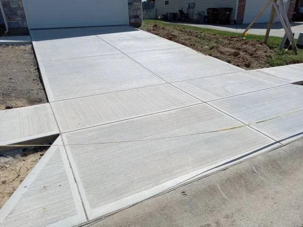 Newly paved concrete driveway and sidewalk leading to a garage, with construction tools and dirt nearby.