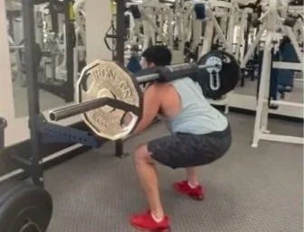 Person performing a squat while lifting a barbell with weights at a gym.