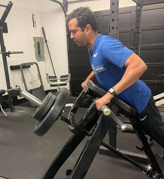 Man in blue shirt using a horizontal barbell leg press machine at gym.