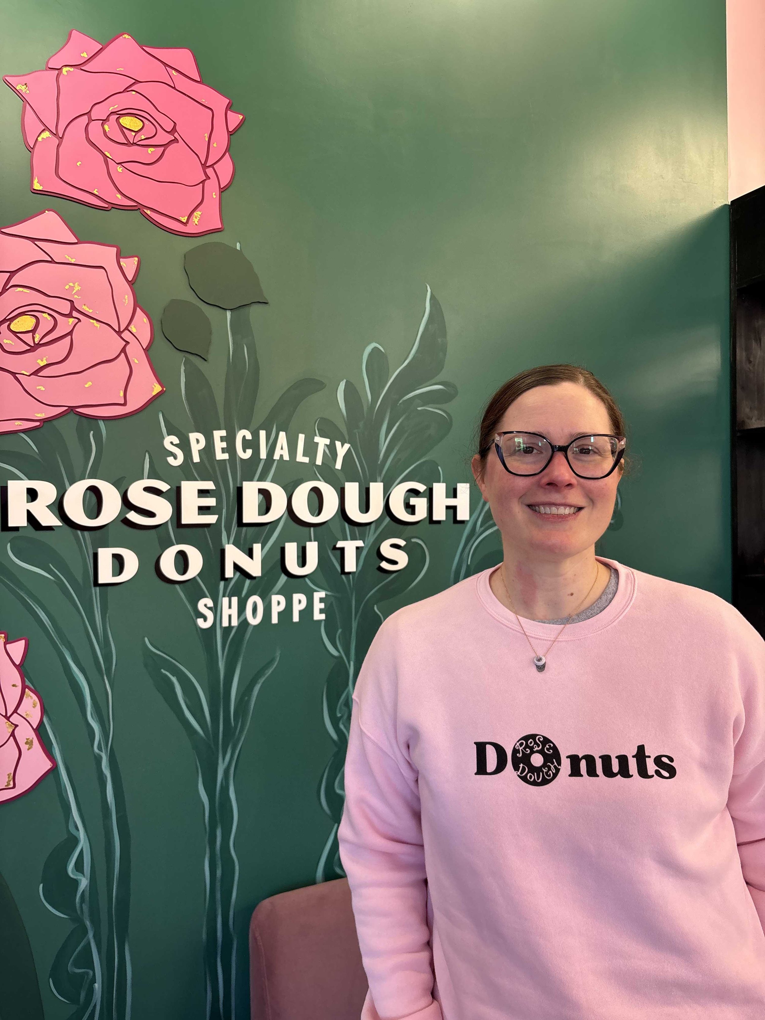 A woman in a sweatshirt that says donut in her doughnut shoppe