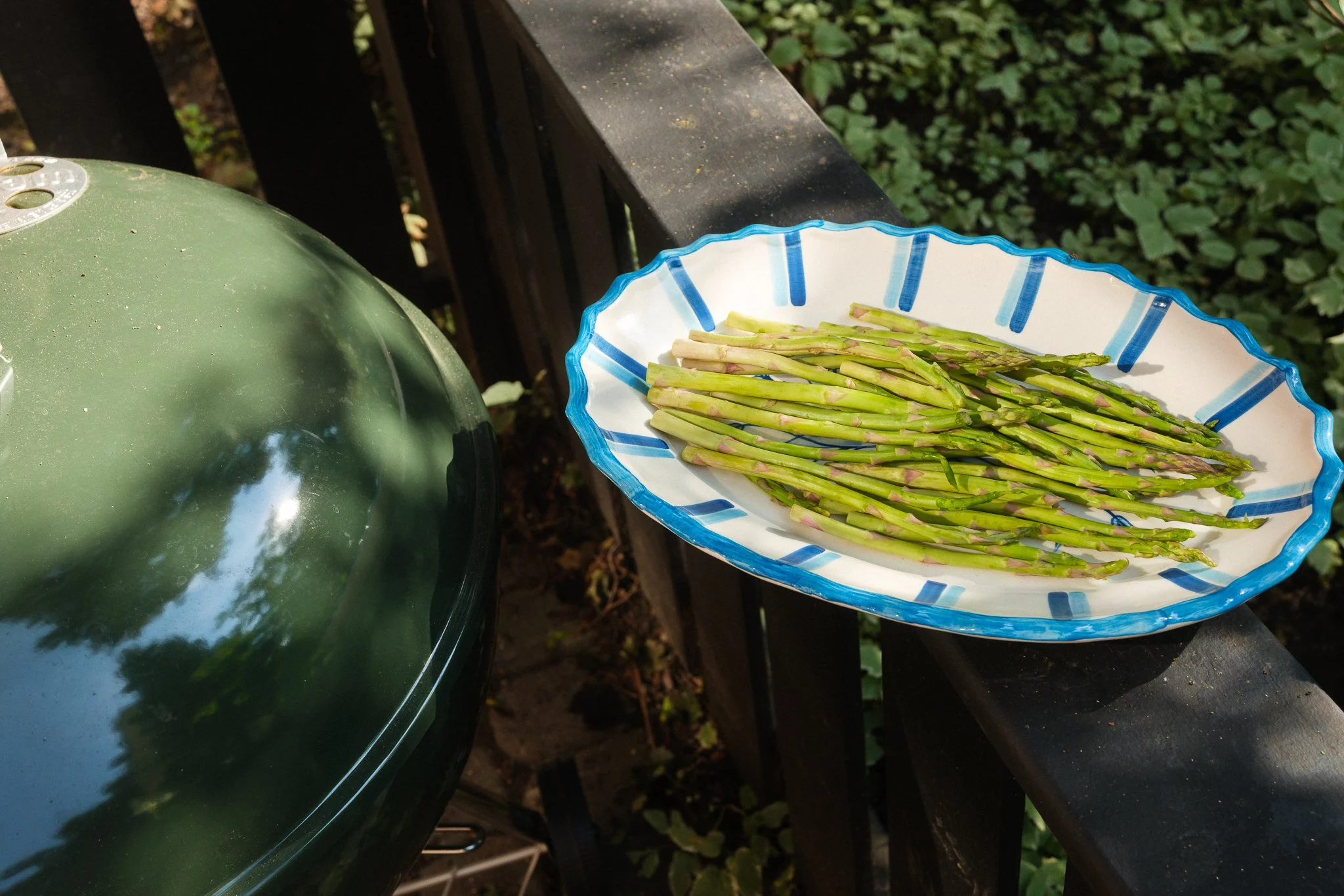 STUDIO PURANI Tulip serving platter in blue holding fresh asparagus on an outdoor grill deck — hand-painted ceramic platter for entertaining