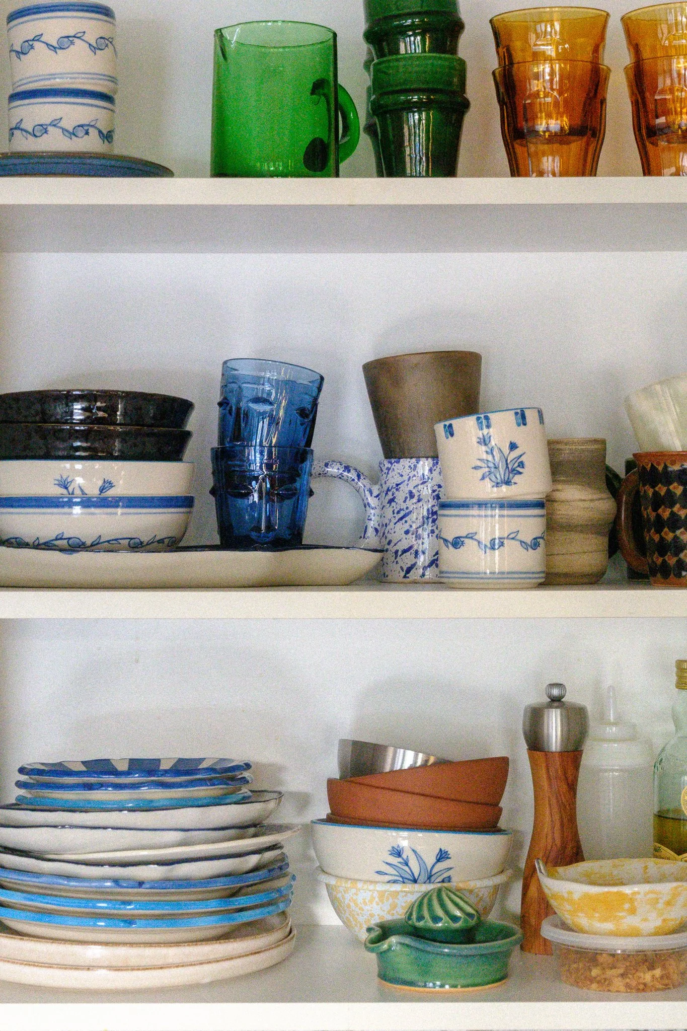 Kitchen cabinet with a mixed dinnerware collection, including STUDIO PURANI Pomegranate and Tulip cups, bowls, and plates