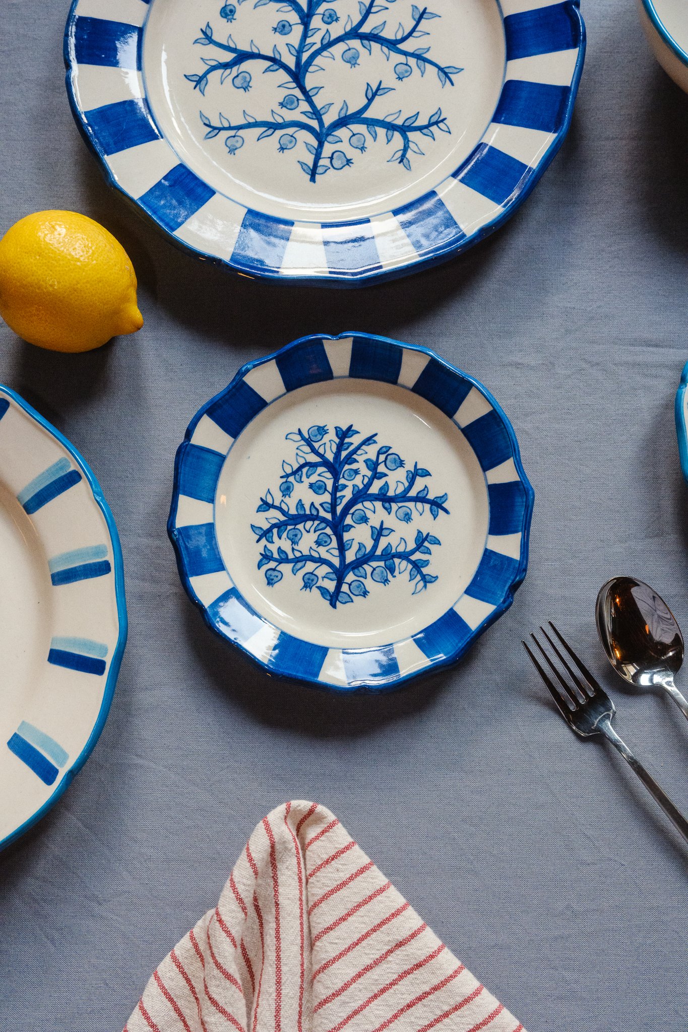 STUDIO PURANI Pomegranate dessert plate in blue styled with a matching dinner plate, Tulip dinner plate, and lemon — hand-painted blue and white ceramic tableware