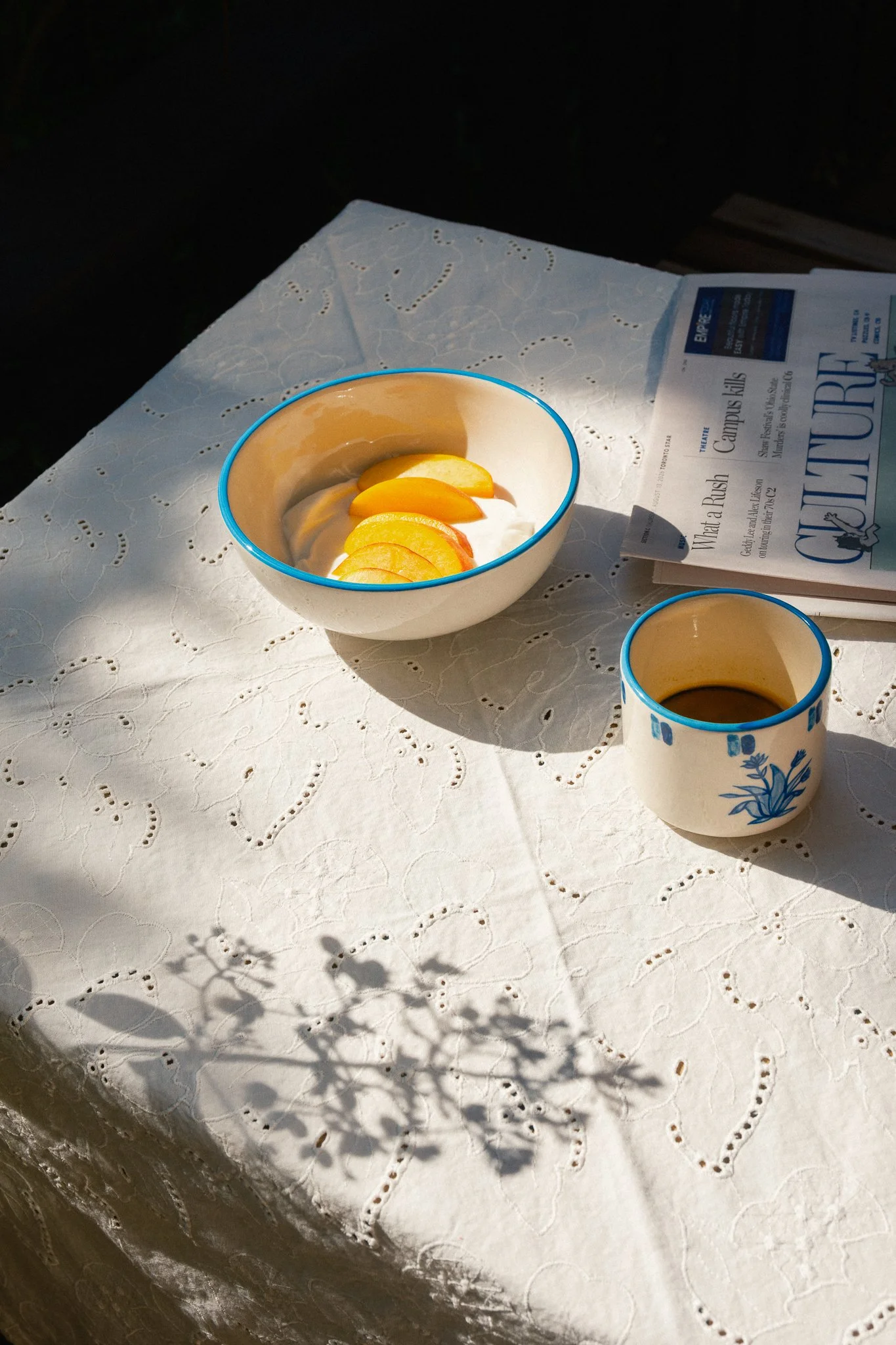 STUDIO PURANI Tulip cappuccino cup in blue with coffee, styled beside a bowl of peaches and yogurt on an eyelet tablecloth — hand-painted ceramic cappuccino cup