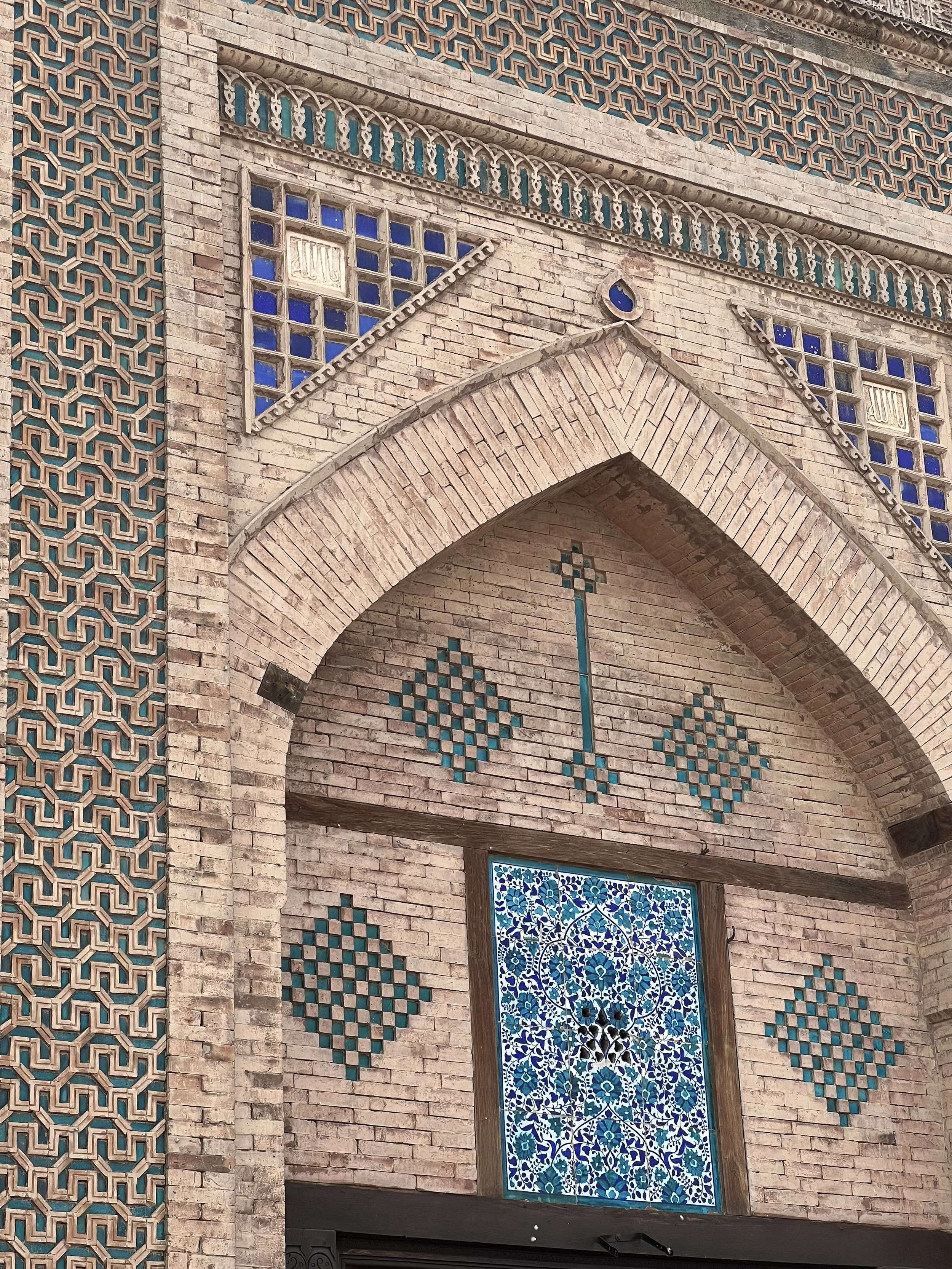 Ornate brick facade with geometric tile patterns and a blue floral stained glass window, seen while visiting artisan workshops in Multan