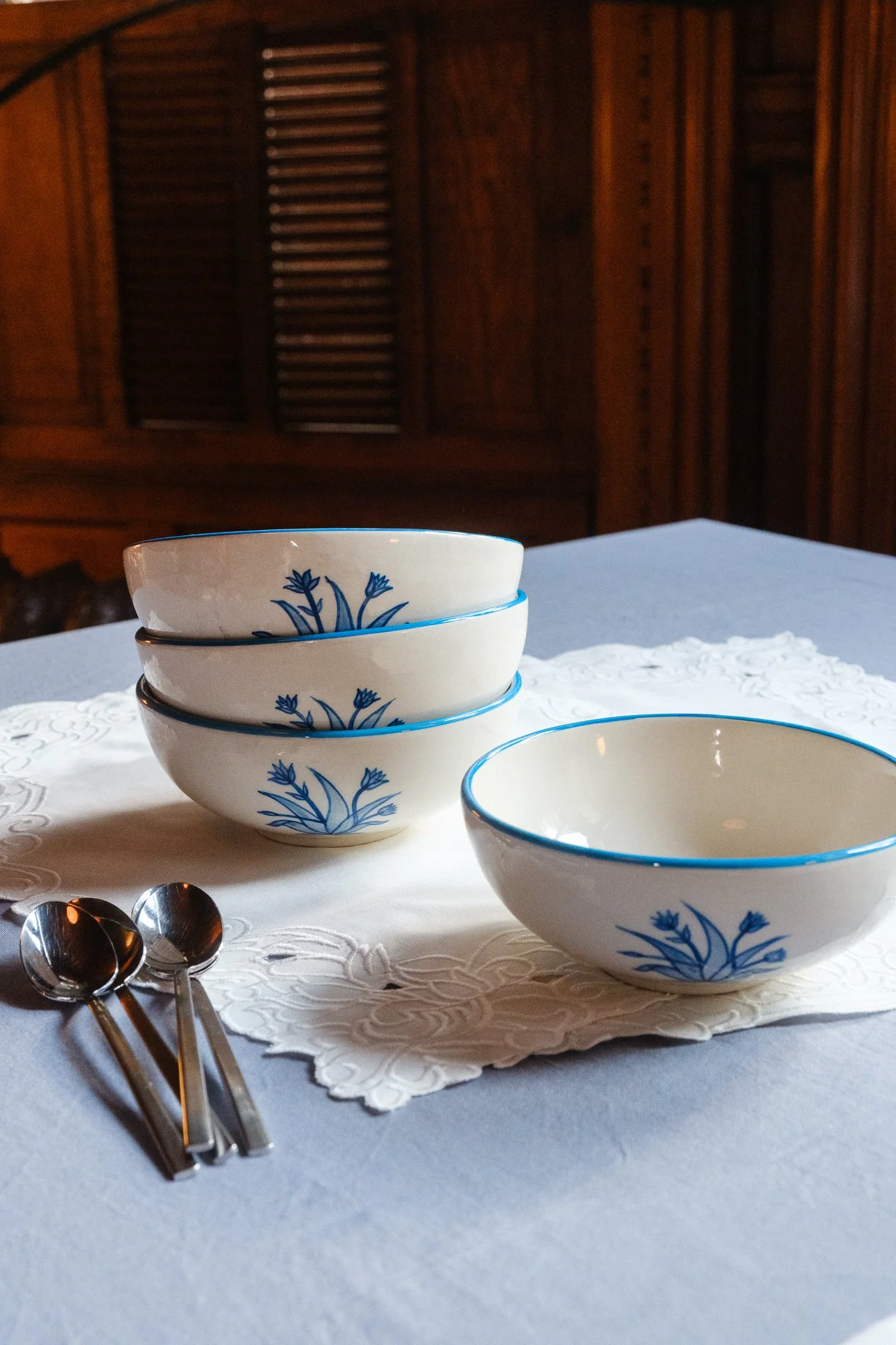STUDIO PURANI Tulip breakfast bowls in blue stacked on embroidered placemats with spoons — hand-painted ceramic bowls with tulip design