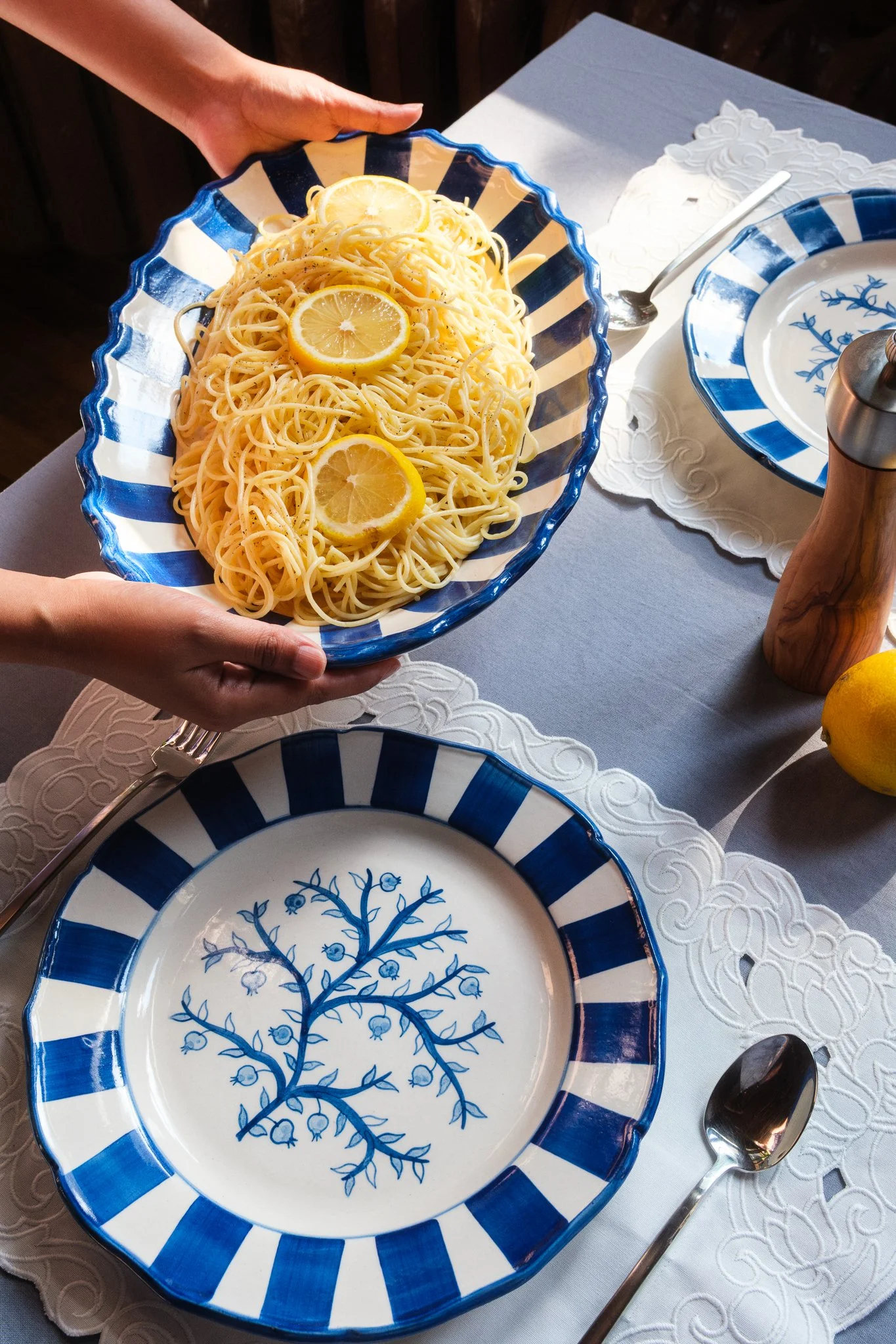 STUDIO PURANI Pomegranate serving platter in blue holding lemon spaghetti, styled with a matching Pomegranate dinner plate, spoon, and pepper mill — hand-painted ceramic platter for entertaining