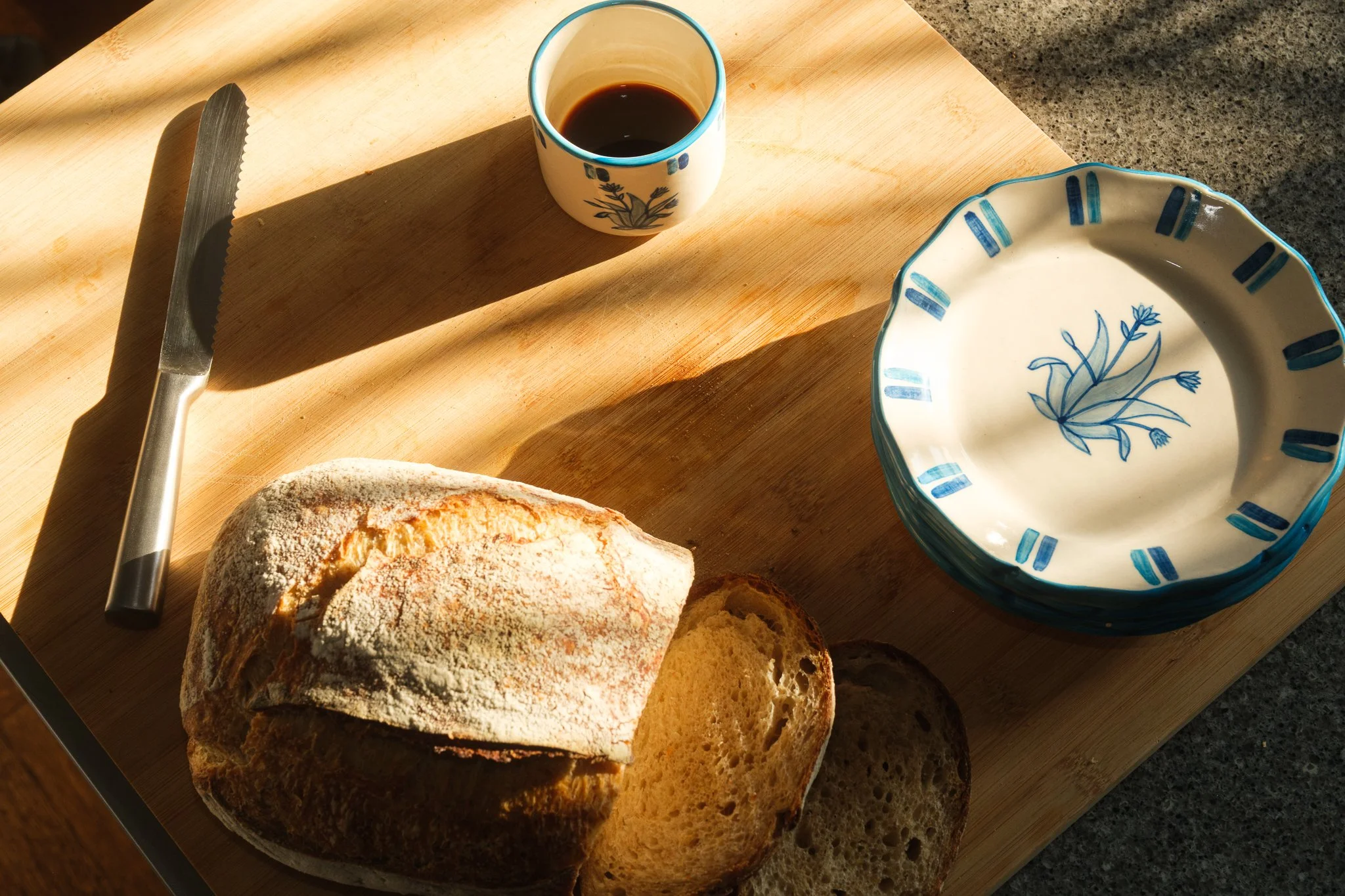 STUDIO PURANI Tulip cappuccino cup in blue filled with coffee, styled with sourdough bread and matching Tulip dessert plates — hand-painted ceramic cappuccino cup