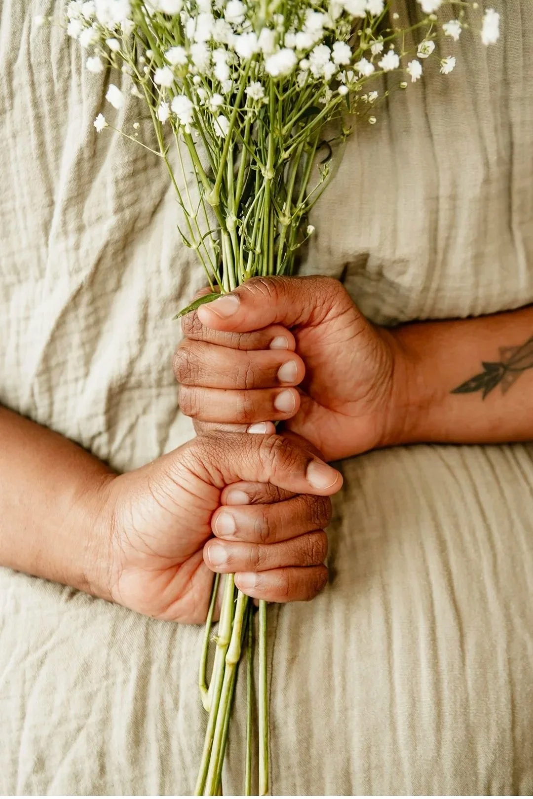 Person holding a bouquet of small white flowers with both hands, against a beige and cream-colored fabric background.