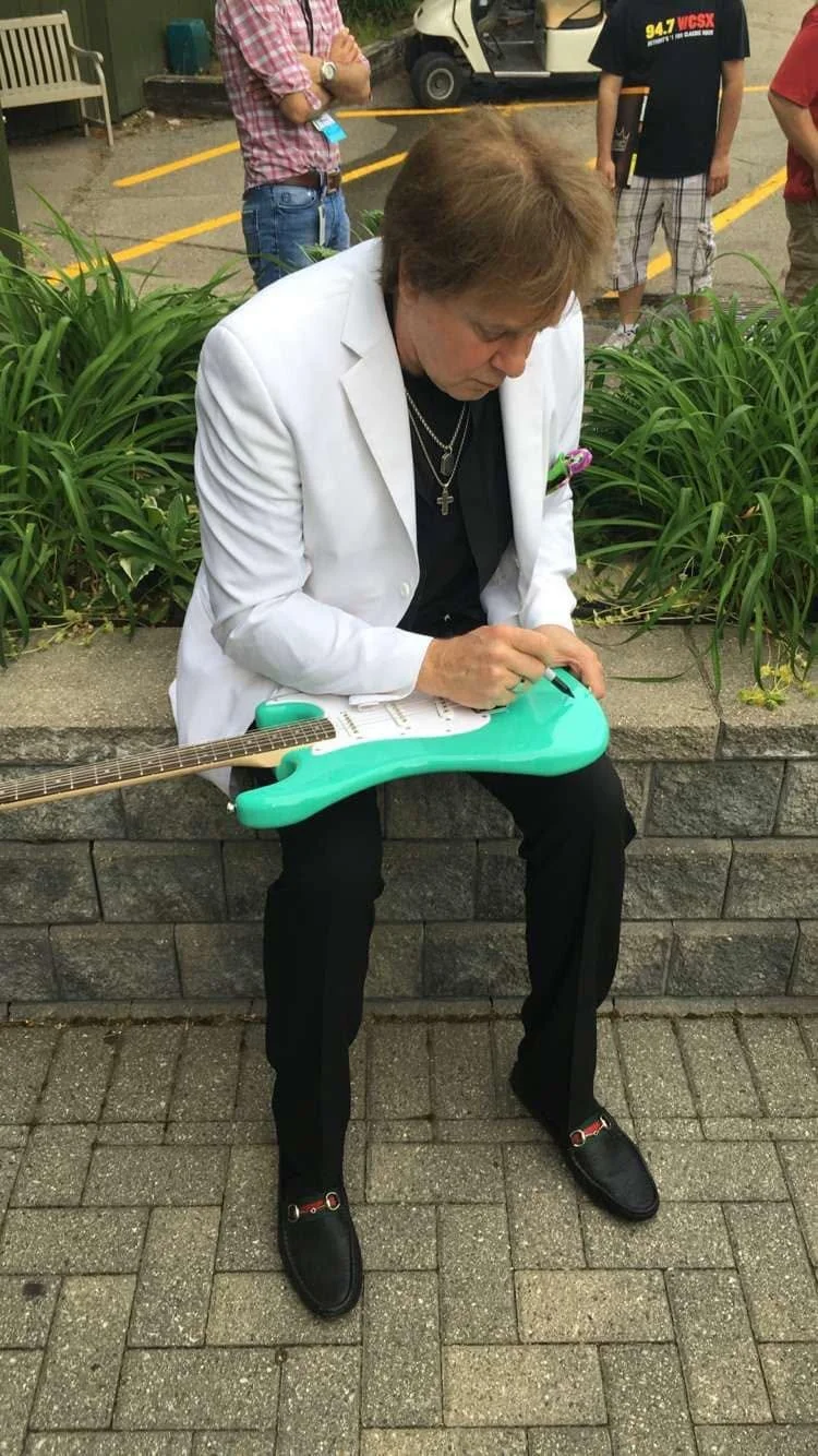 Eddie Money signing the guitar with his autograph