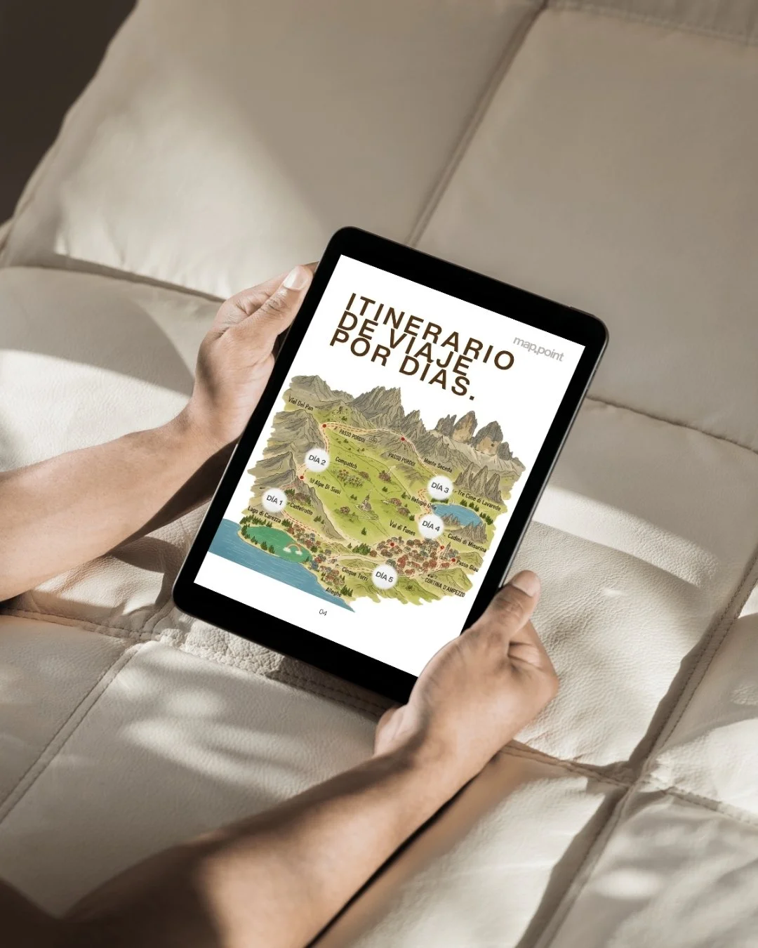 Una persona sosteniendo una tableta con un mapa ilustrado de un itinerario de viaje de varios días en un sofá beige.