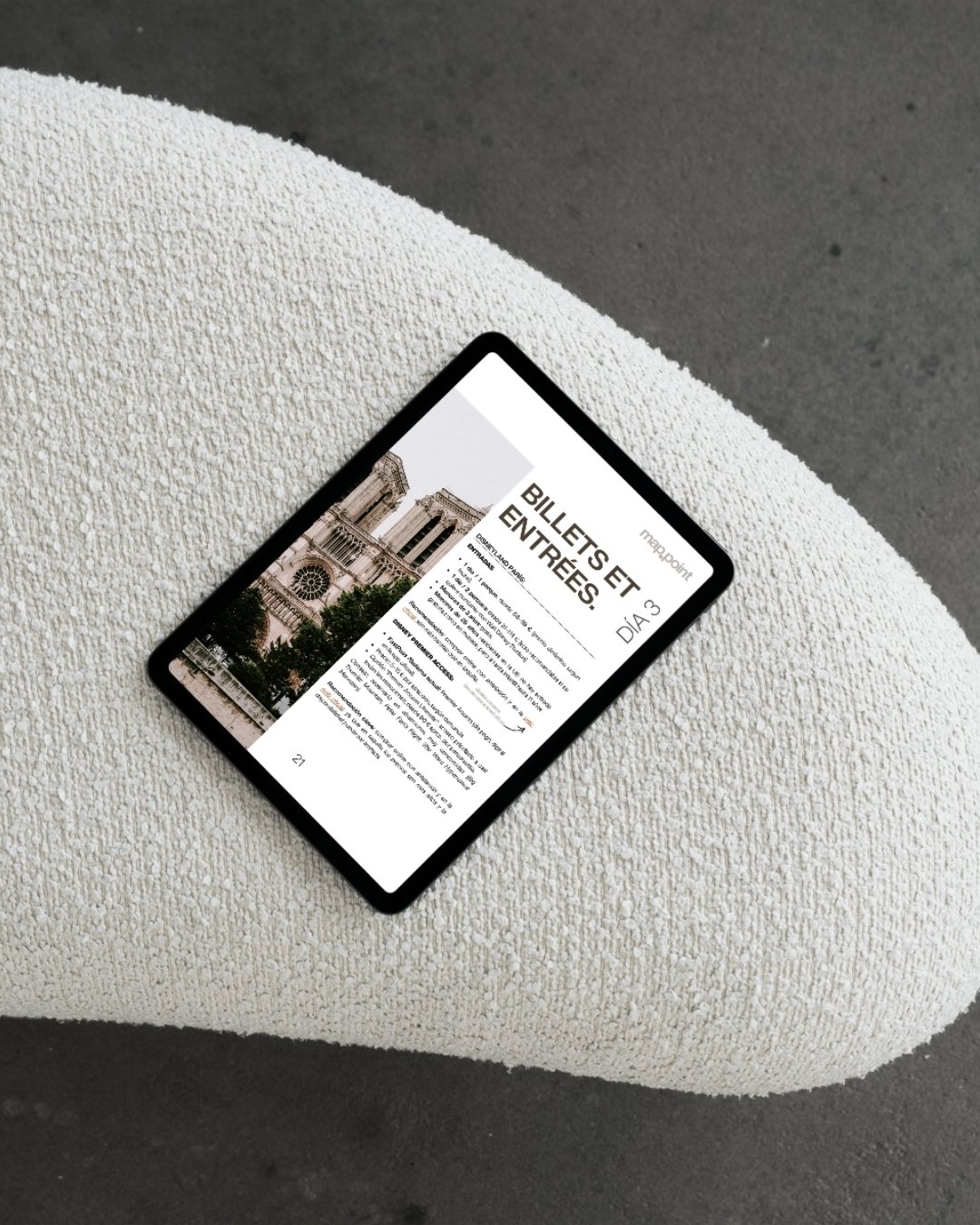 Una tableta digital sobre una superficie de color claro muestra billetes y entradas para un día en París, con una imagen de una catedral antigua en la pantalla.