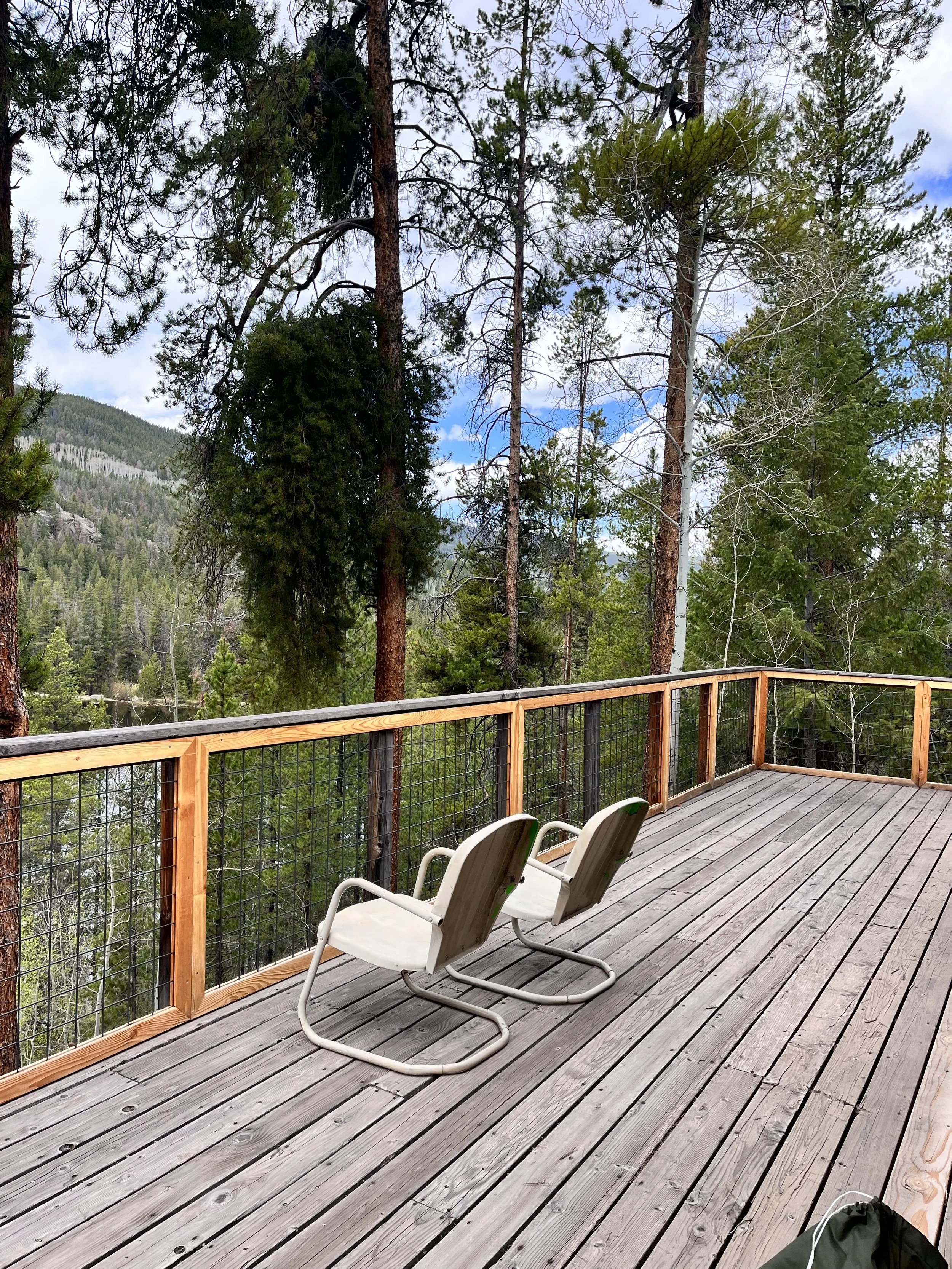 Deck with two white chairs overlooking a forested mountainous landscape with trees and blue sky.