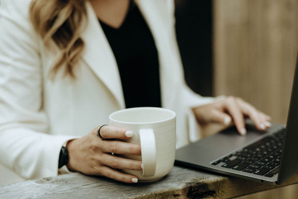 Woman in white blazer holding a mug while using a laptop