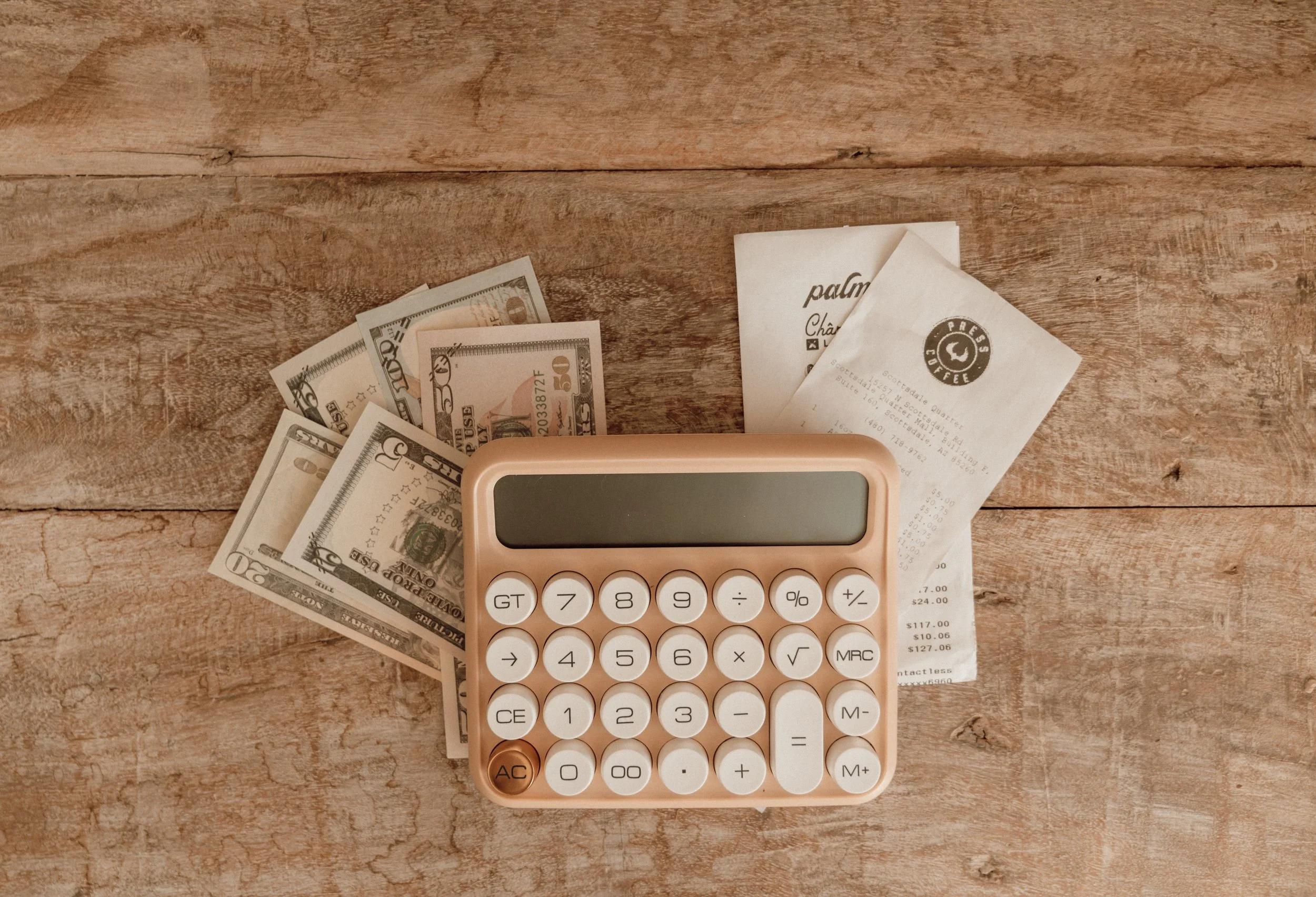 Calculator, US dollar bills, receipts on wooden table.