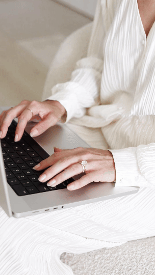 Woman in white dress typing on a laptop, wearing a ring