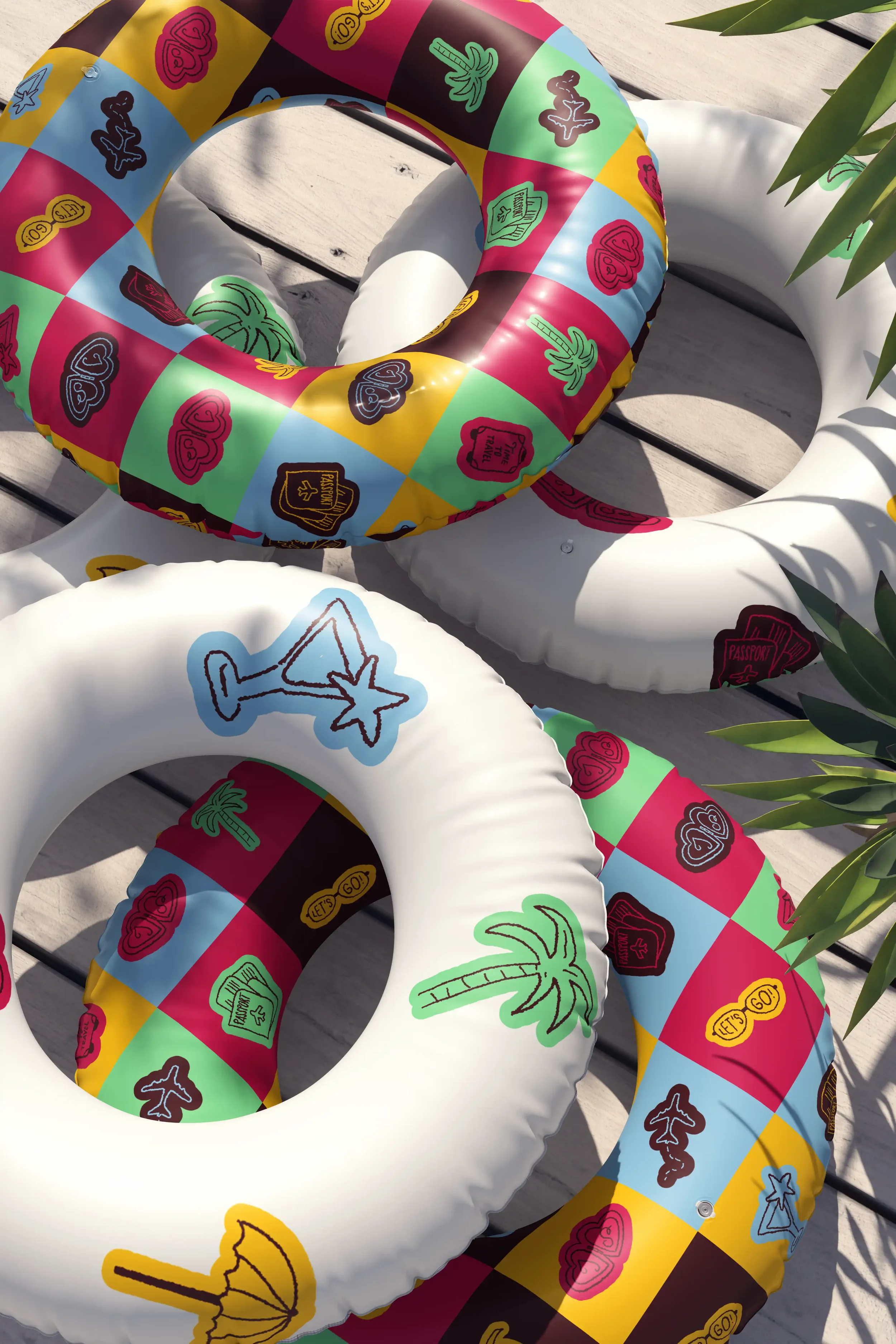 Des bouées de piscine en forme de rond, décorées avec des motifs de palmiers, d'images de cocktail, de cœurs et de passeports, posées sur un sol en bois, avec des feuilles de plante verte à droite.