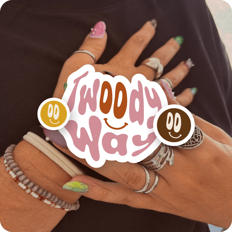 Main avec plusieurs bijoux, ongles décorés, et une sticker avec le texte 'Twoody Way' sur la main.