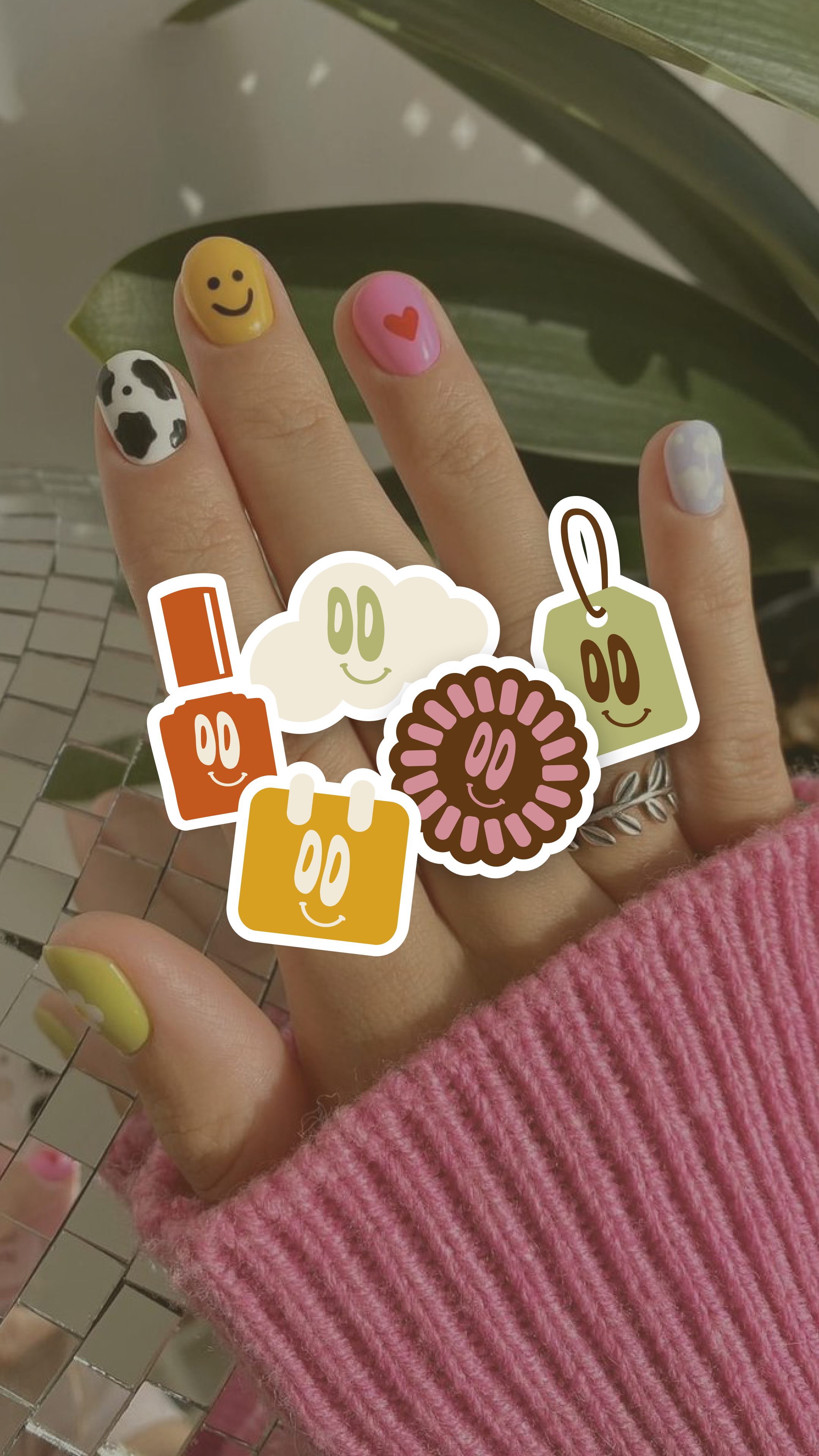 Doigts avec ongles peints de différentes couleurs et motifs, accompagnés de stickers de formes diverses avec des visages souriants.