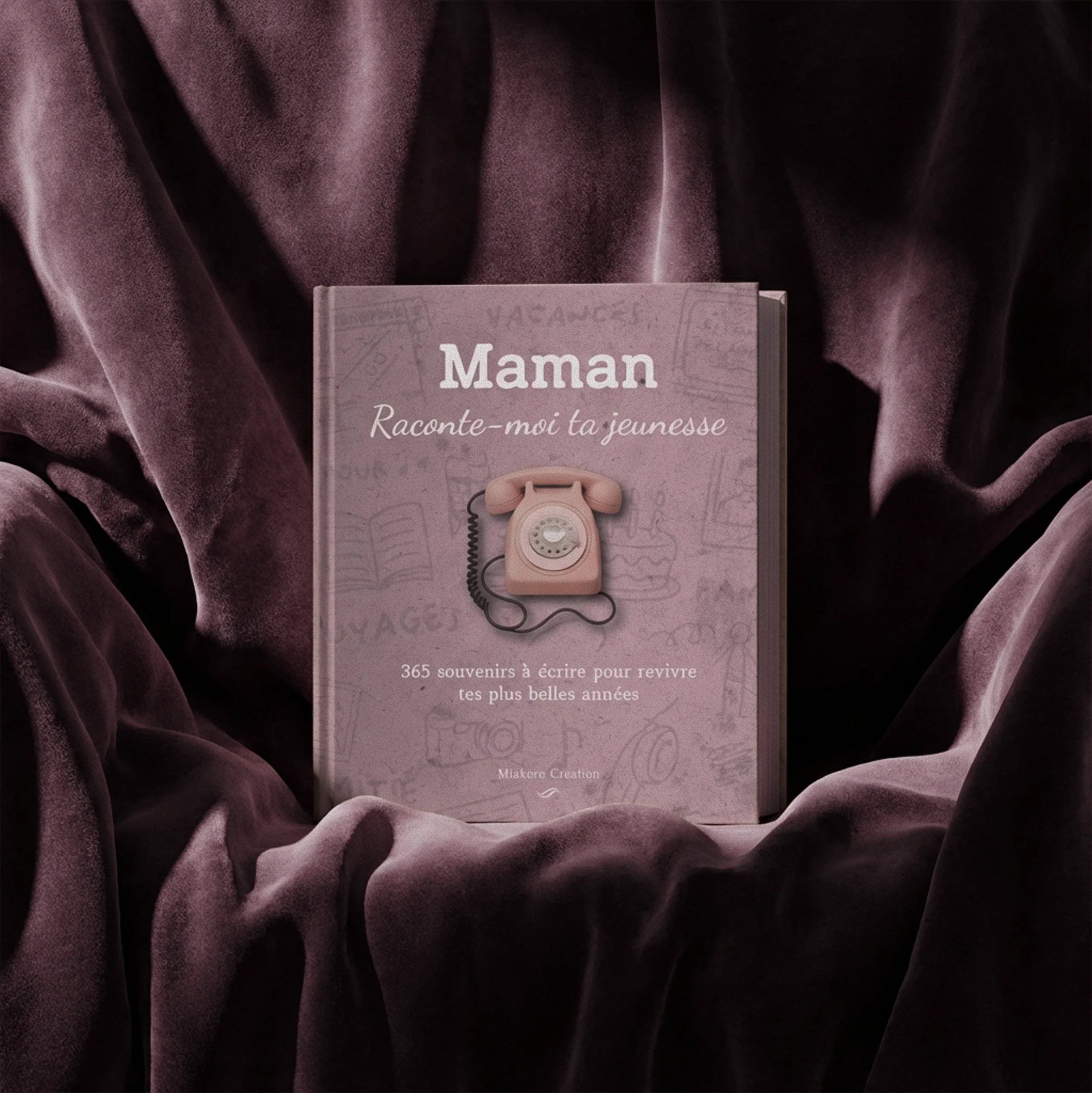 Un livre rose intitulé "Maman Raconte-moi la jeunesse" est posé sur un tissu violet foncé, avec une illustration d'un téléphone rétro en relief sur la couverture.