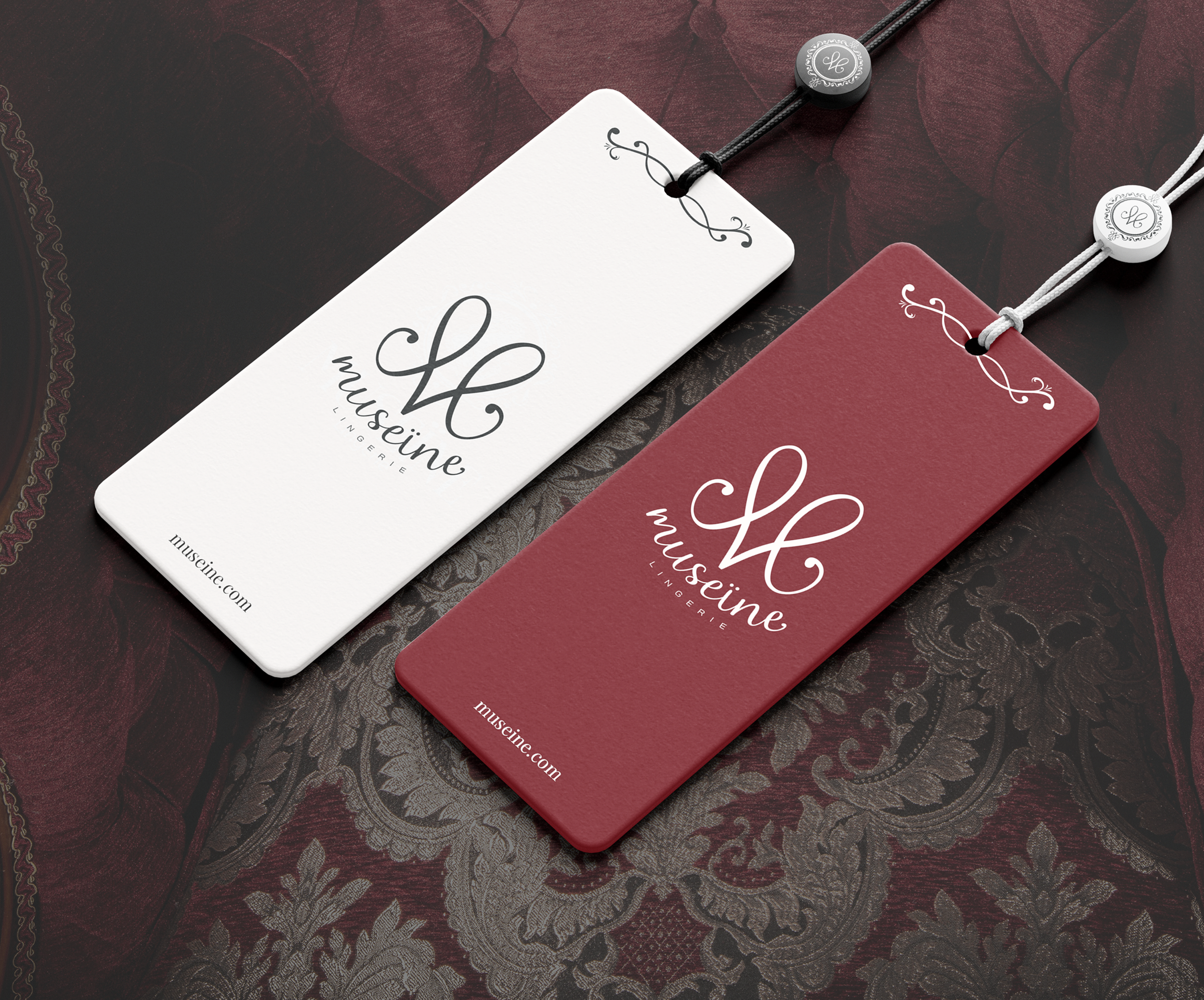 Deux étiquettes de lingerie de la marque Museine, l'une blanche et l'autre rouge, posées sur un tissu à motif floral. Les étiquettes ont un logo élégant en cursive avec le nom de la marque et le site web museine.com.