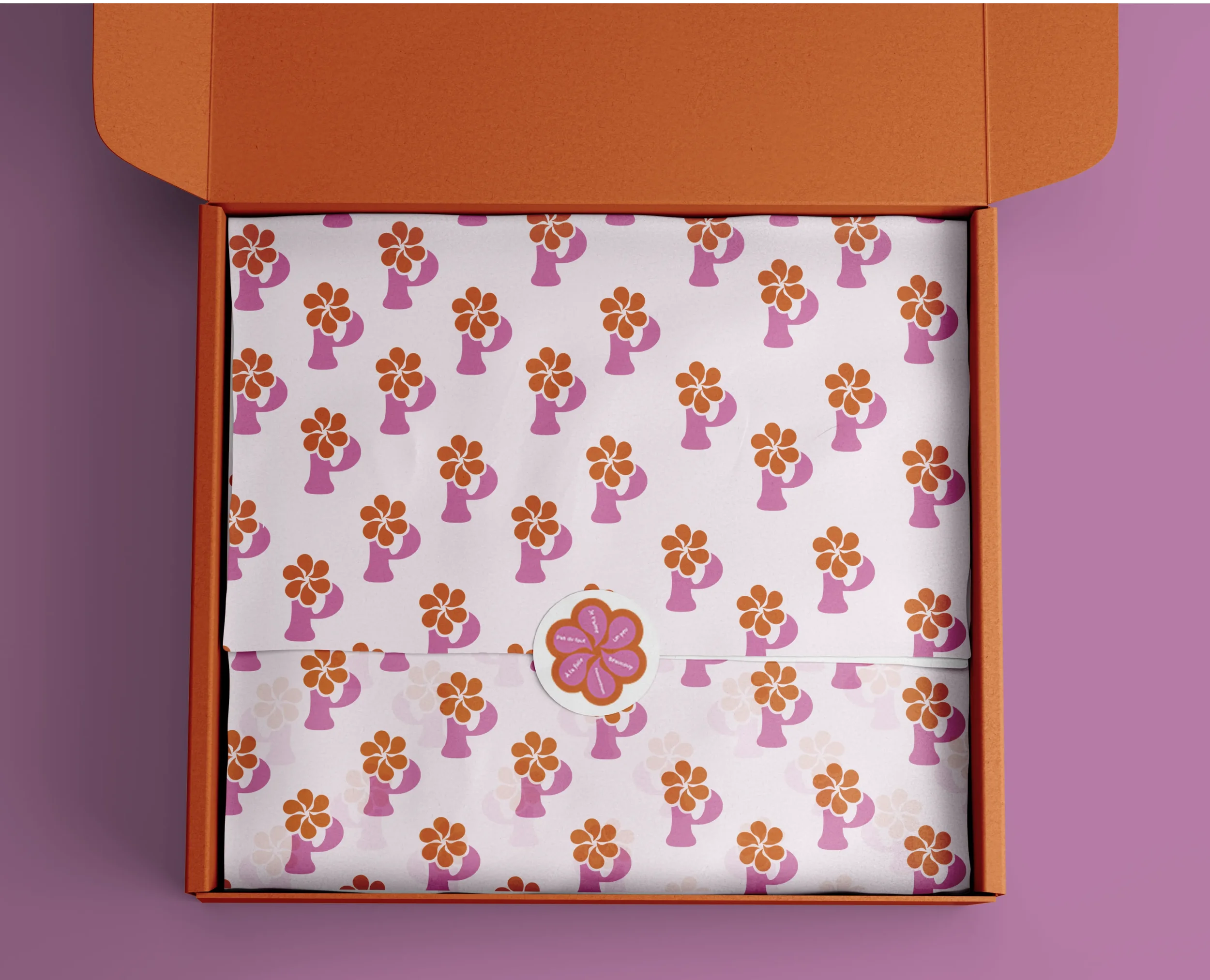 Une boîte orange contenant deux papiers décorés de motifs floraux violets et oranges, avec un autocollant floral au centre.