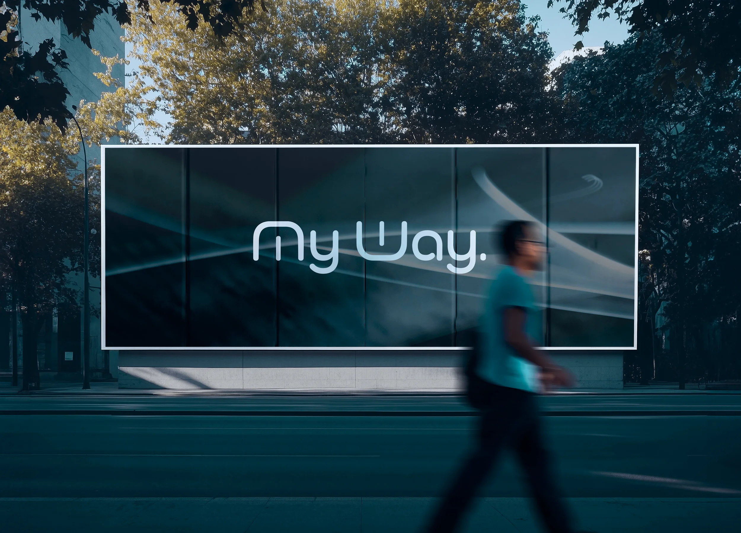 Une grande affiche numérique avec le texte  my Way  est visible. Un homme marche devant l'affiche, flou en raison du mouvement. L'arrière-plan montre des arbres et un ciel en début de soirée ou tôt le matin.