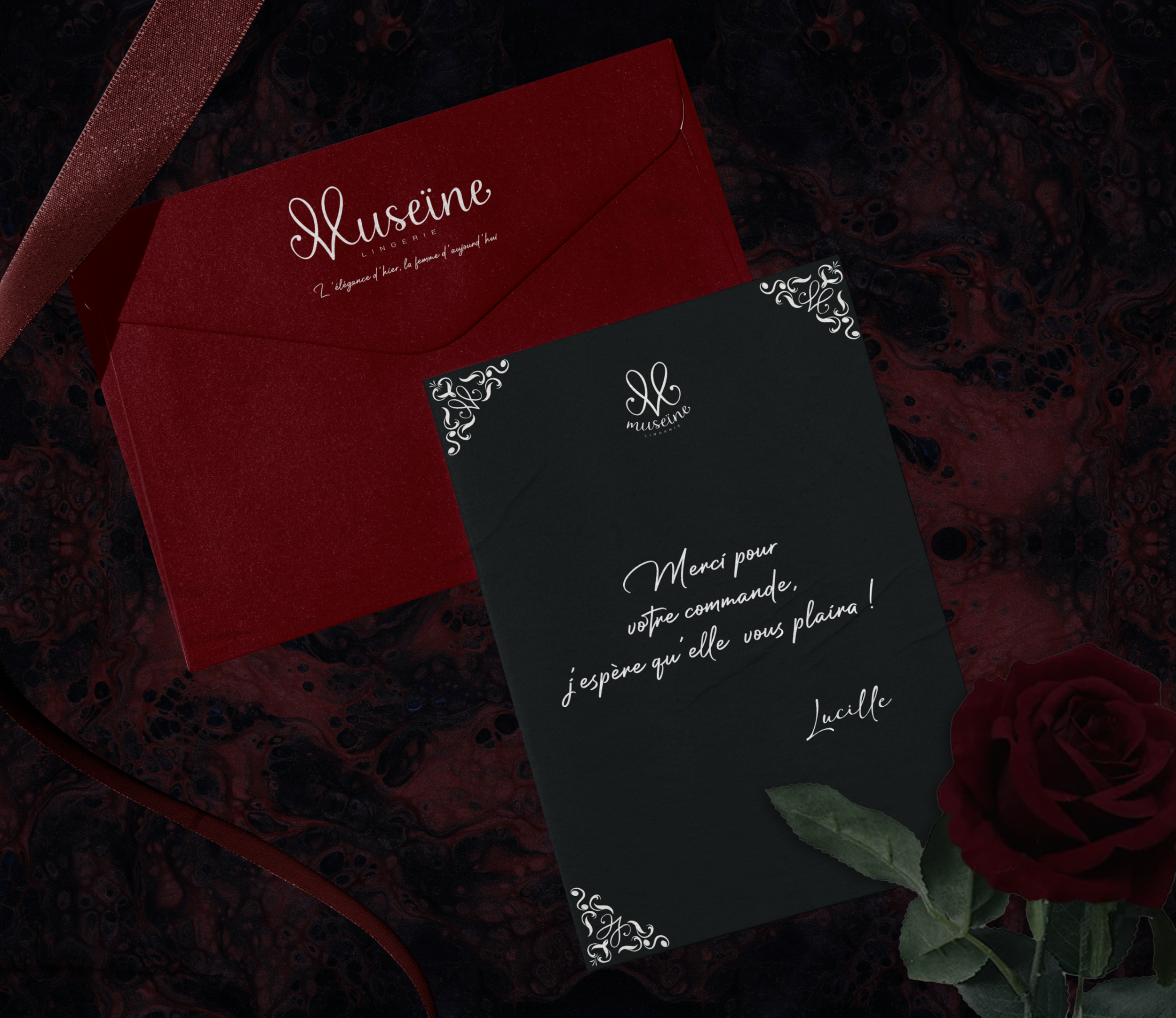 Une carte de remerciement noire avec le logo 'Museine' en haut, accompagnée d'une rose rouge sur un fond en tissu noir avec des motifs rouges et une bande de satin rouge. La carte porte un message en français de Lucille, remerciant pour une commande 