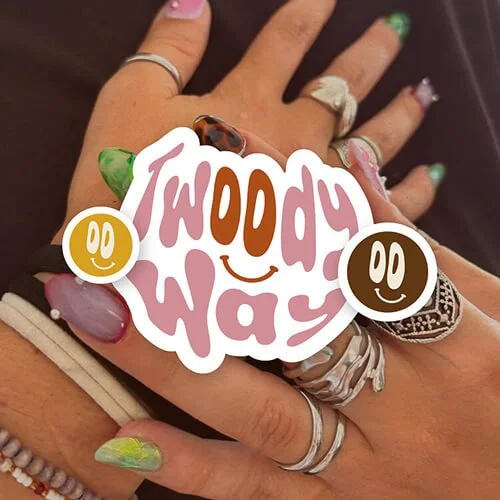 Une main avec plusieurs bagues et ongles colorés, tenant un autocollant avec le texte 'Today is a good day' et deux smileys.