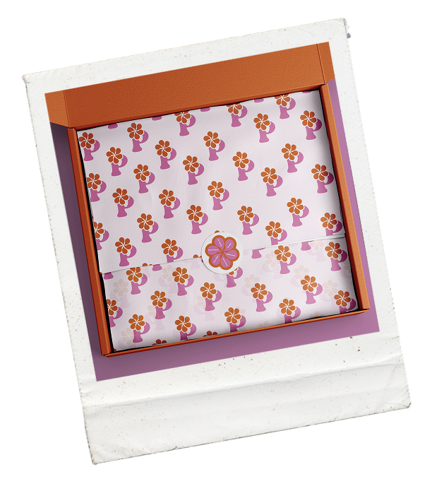 Coffret cadeau ouvert avec papier de soie décoré de fleurs orange et violette, contenant un objet central en forme de fleur.