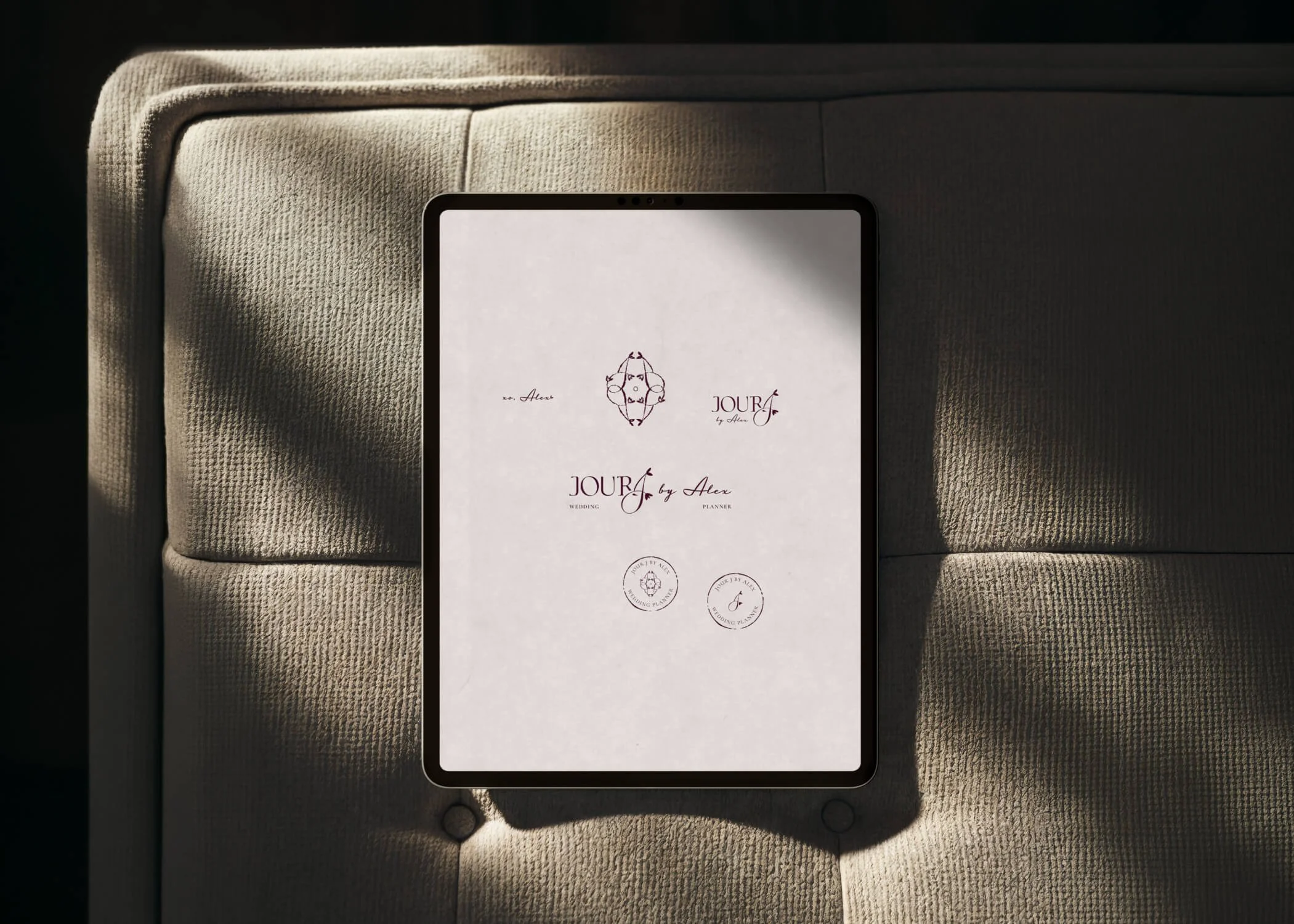 Une tablette numérique affichant un document avec les logos de Jour j by Alex, une Wedding planner, reposant sur un revêtement en tissu beige.