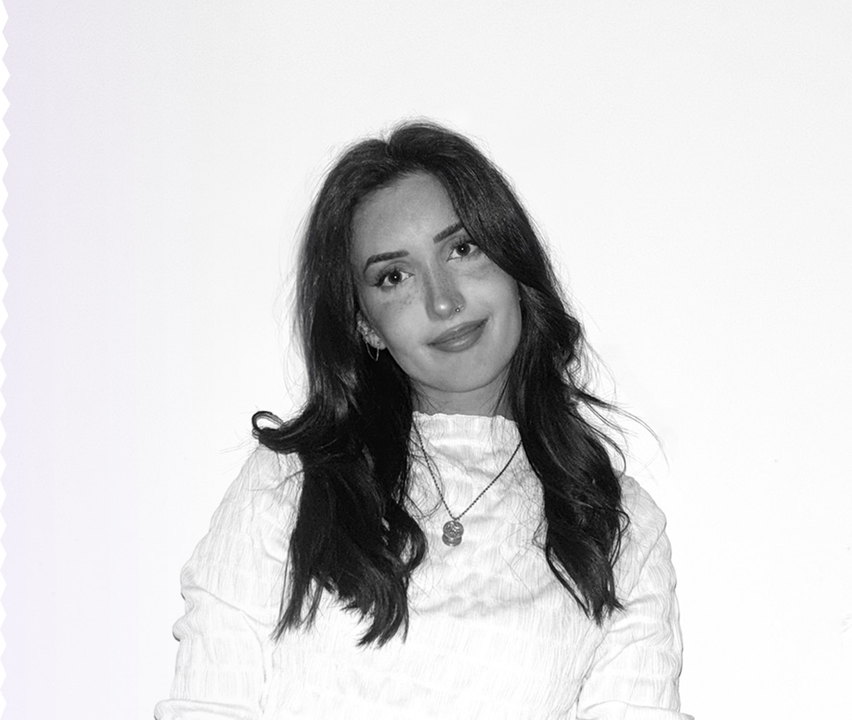 Portrait en noir et blanc d'une femme avec des cheveux longs et bouclés, portant un haut à manches longues et un collier, souriant légèrement.