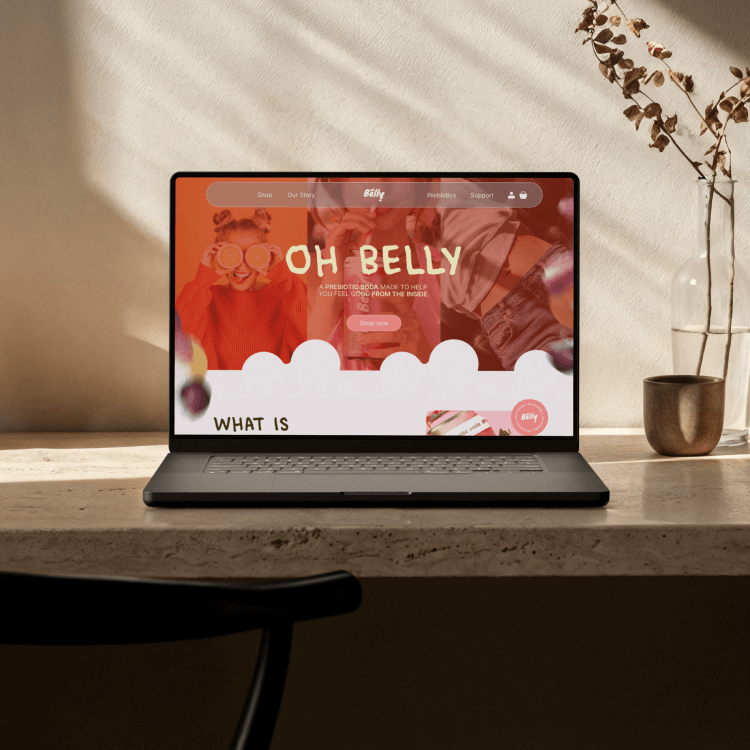 Ordinateur portable sur un bureau avec une page web ouverte intitulée "Oh Belly" et une décoration simple avec une vase et des branches.
