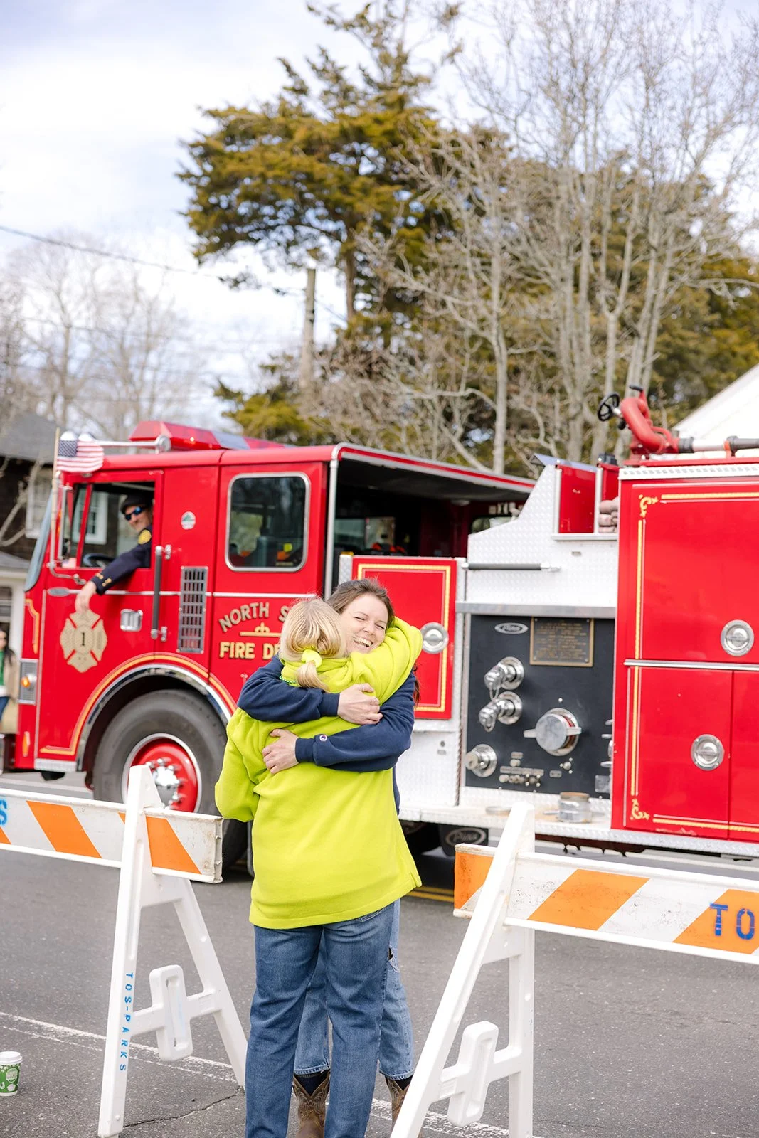 A firefighter hugs a young girl in front of a red fire truck during a community event.