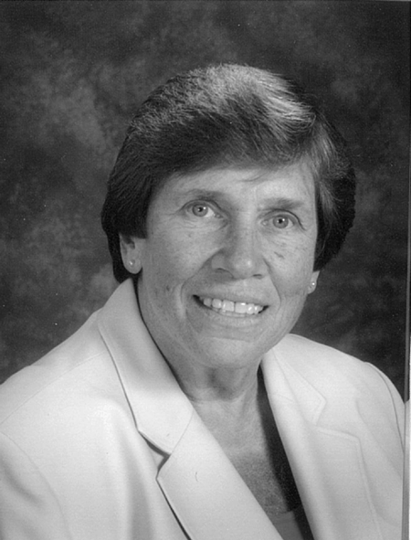 Black and white portrait of a smiling middle-aged woman with short, dark hair, wearing a light-colored jacket and a dark top underneath.