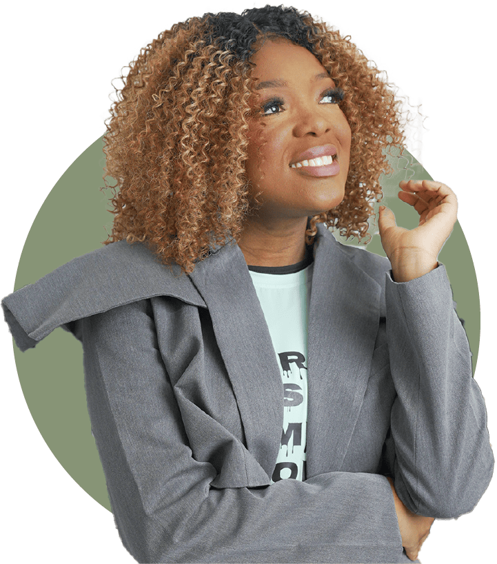 A woman with curly hair and light brown skin smiling and looking upward, wearing a gray blazer over a graphic T-shirt, with one hand near her face.