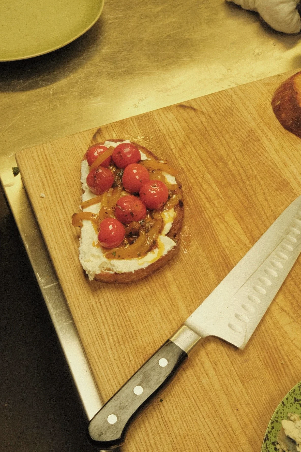 A slice of bread topped with cream cheese, cherry tomatoes, caramelized onions, and herbs on a wooden cutting board.