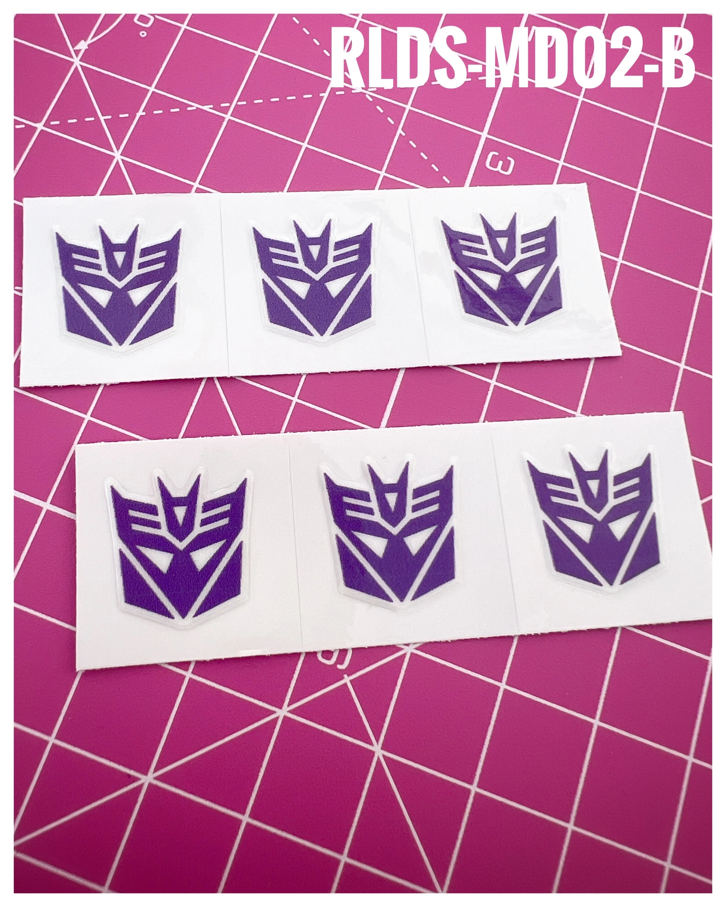 6 x medium toy style Con dry rub transfers, Purple with White background.