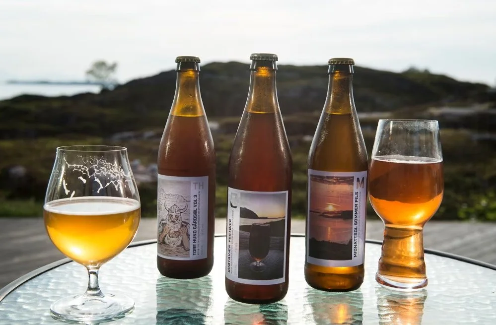Three bottles of beer and two glasses of beer on a glass table outdoors with a natural landscape background.
