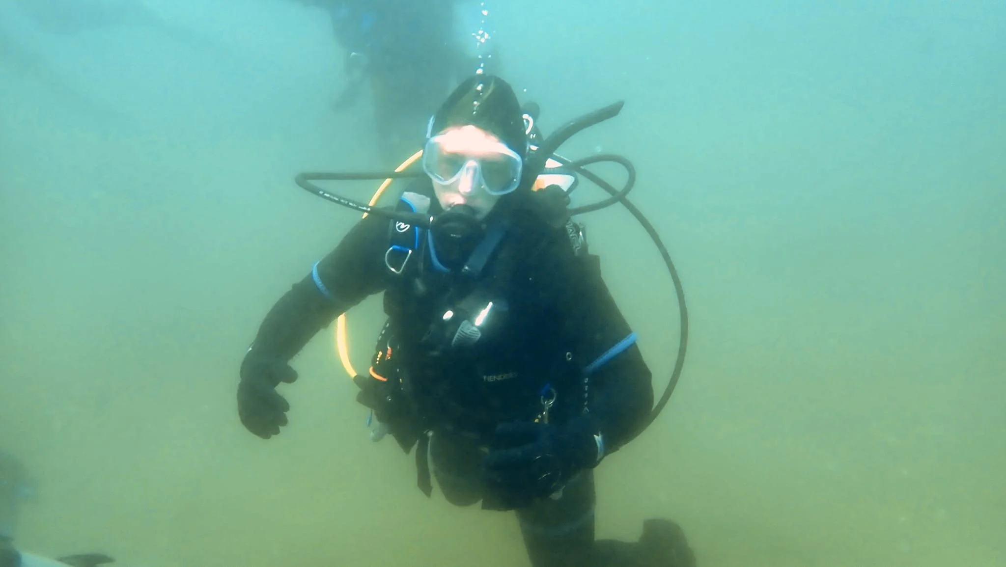 A person scuba diving underwater, wearing a wetsuit, mask, and breathing apparatus, with a yellow hose connected to their tank.