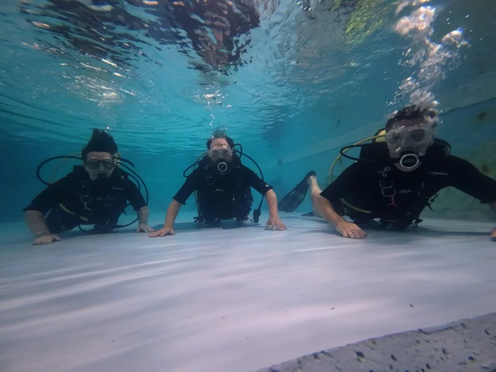 Three people in scuba gear crawling out of a swimming pool.