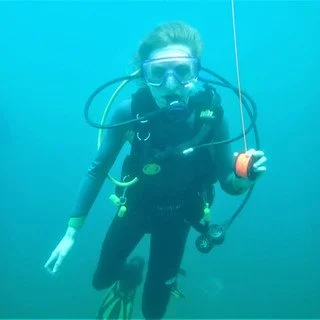Person scuba diving underwater wearing a wetsuit, mask, and oxygen tank