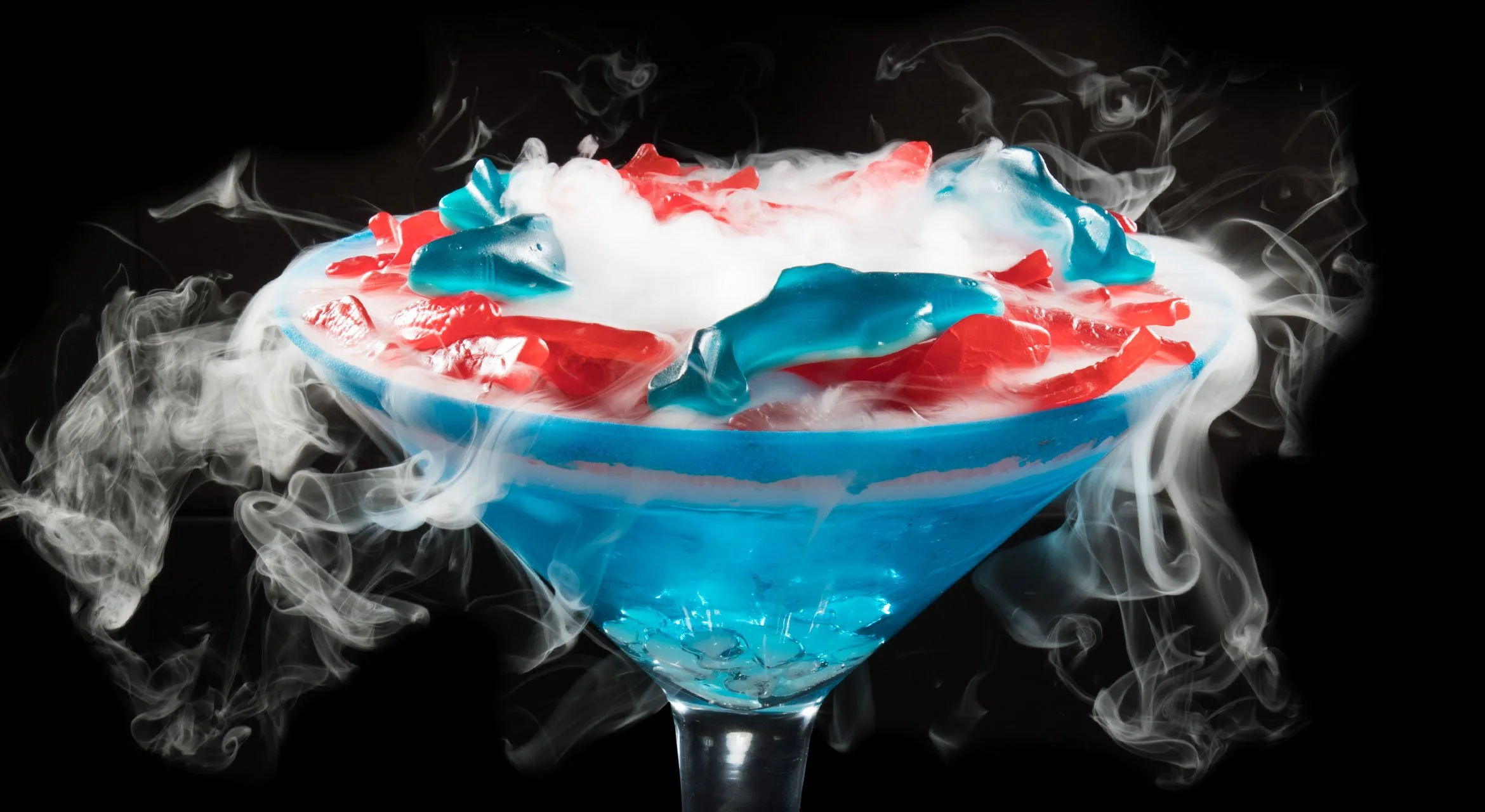 A MILLION FISH IN THE SEA - Smirnoff Red, White, and Berry Vodka, Peach Schnapps, Watermelon Liquor, Blue Curaçao, Pineapple Juice, Sprite - Topped with gummy fish and sharks. Rimmed with blue raspberry Pucker Powder.