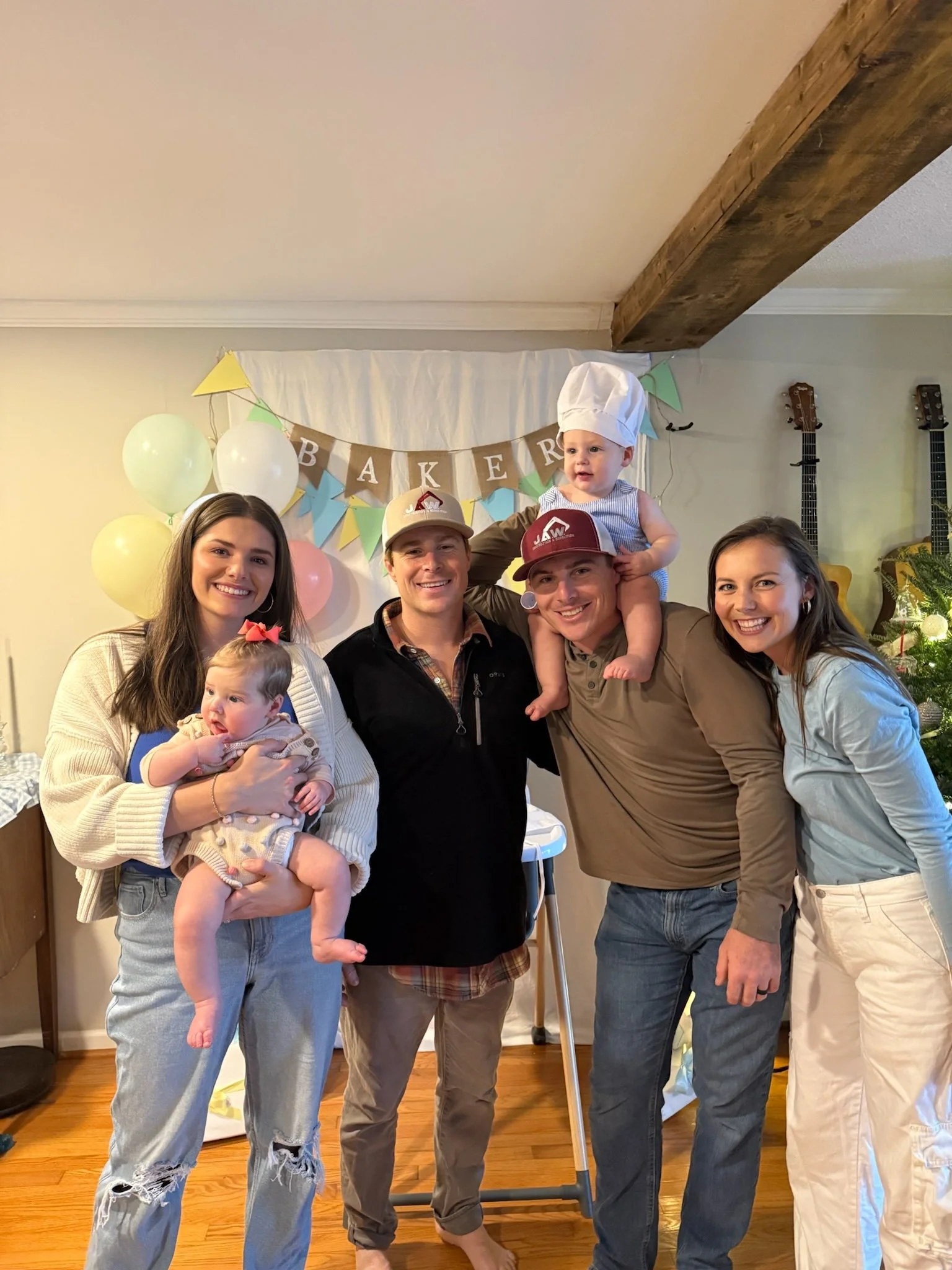 Family celebrating a birthday with balloons and a banner that reads 'Bakers' in a decorated room.