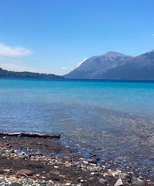 Vista de un lago con aguas tranquilas, rodeado de montañas y un cielo eterno.